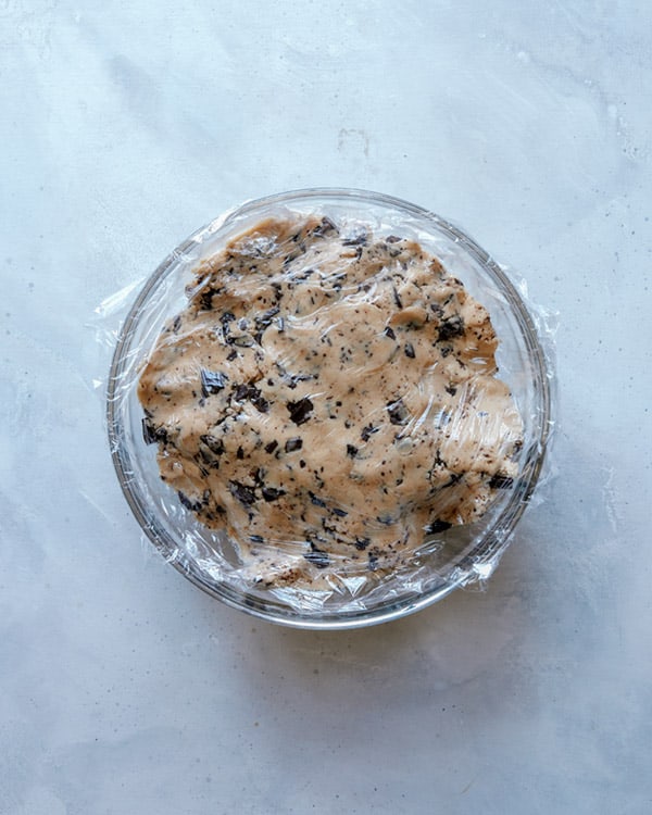 Chocolate chip cookie dough in a bowl with plastic wrap.