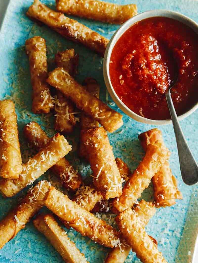 Wonton mozzarella sticks on a platter with marinara sauce on the side.