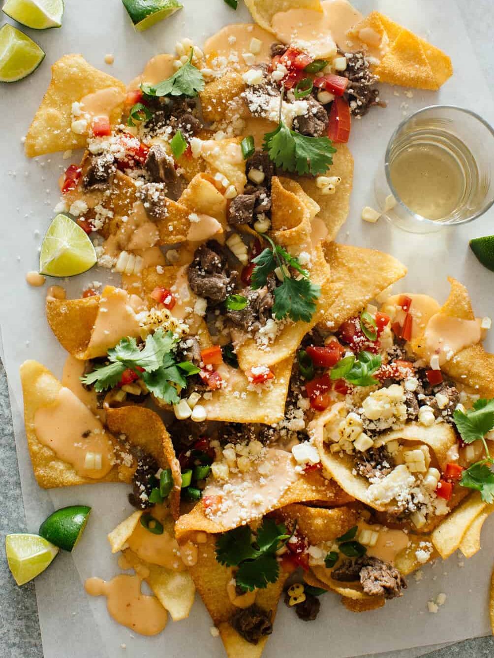 Korean BBQ nachos with lime wedges and a drink for a Super Bowl appetizer. 