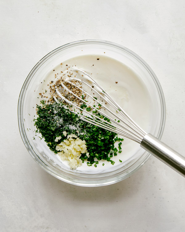 Herbs into the base of ranch dressing in a glass bowl.