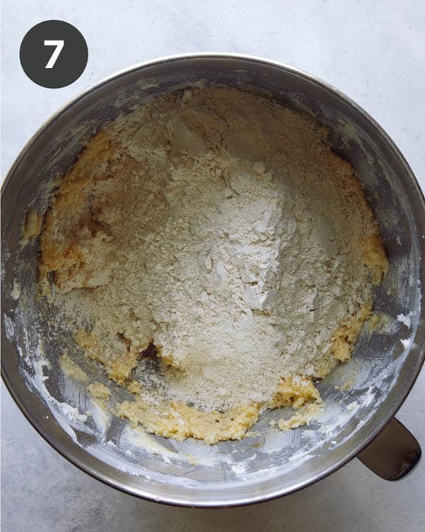 Flour being added to sugar and butter in the well of a stand mixer.