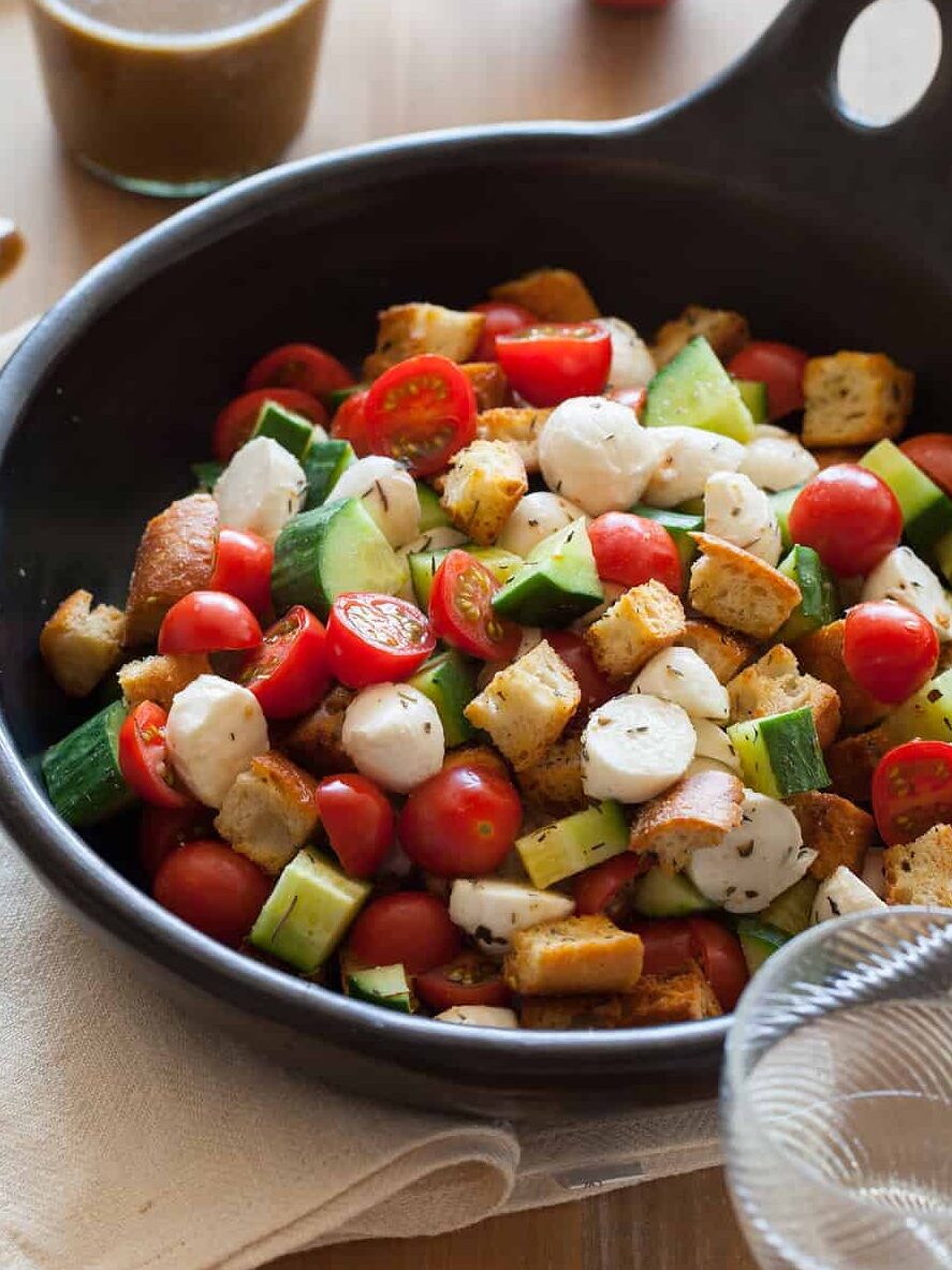 Panzanella salad in a serving bowl with a jar of dressing and a spoon.