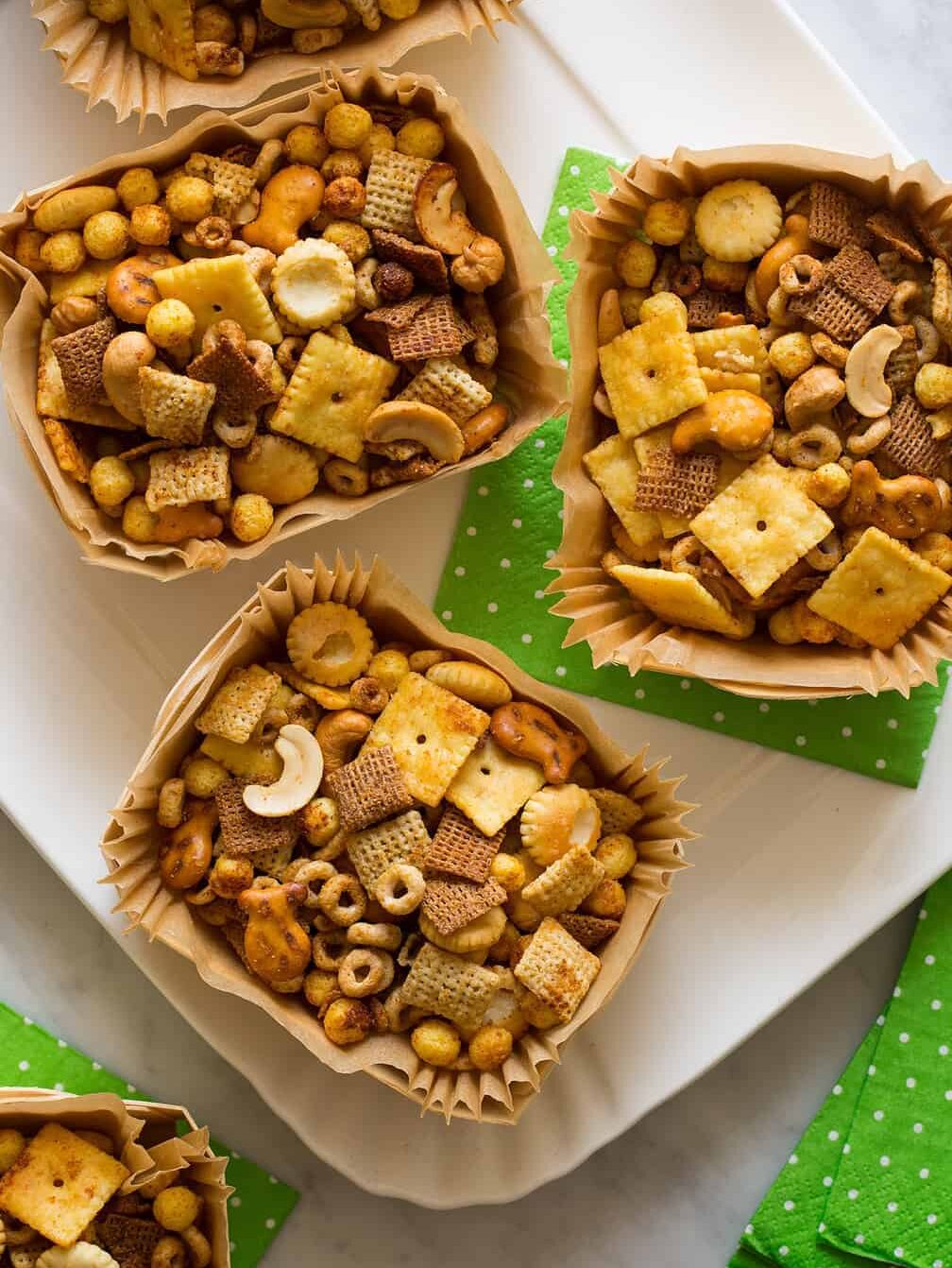 Wood and paper containers full of snack mix on a platter with green paper napkins. The ultimate Super Bowl finger food idea.