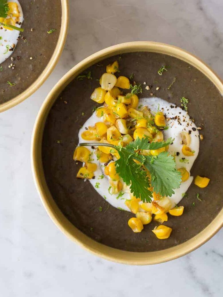 Bowls of spicy black bean soup garnished with sour cream, roasted corn, and cilantro.