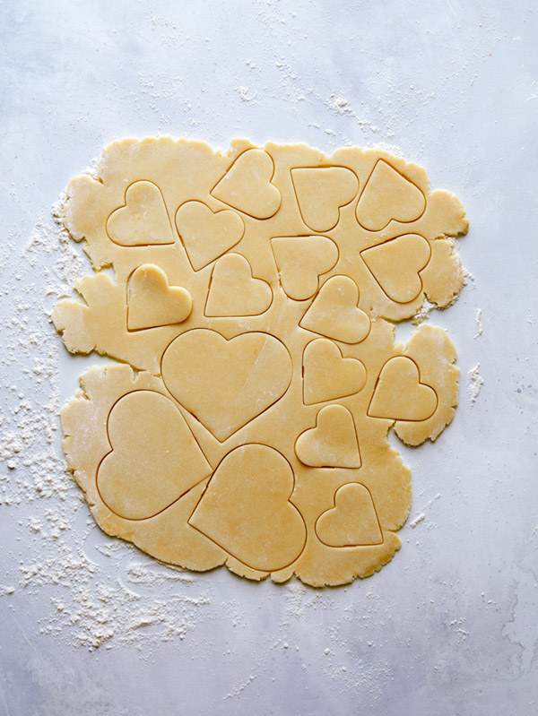 Cookie dough being rolled cut into heart shapes. 