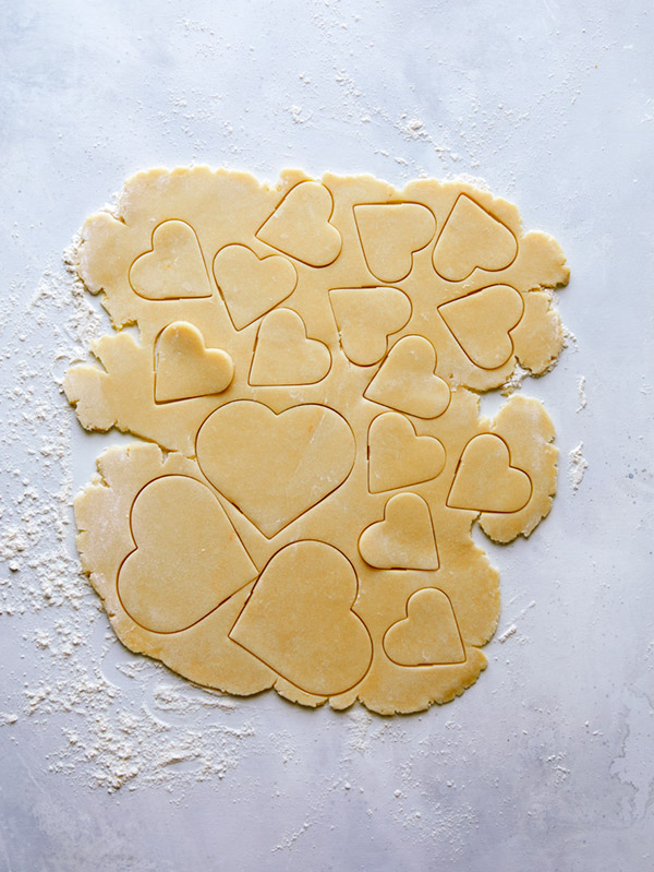 Cookie dough being rolled cut into heart shapes.