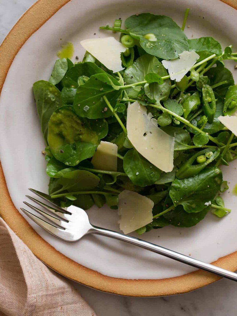 A close up of a plate of watercress salad with green apple vinaigrette and a fork.