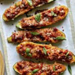 Zucchini boats on a platter with basil on the side.
