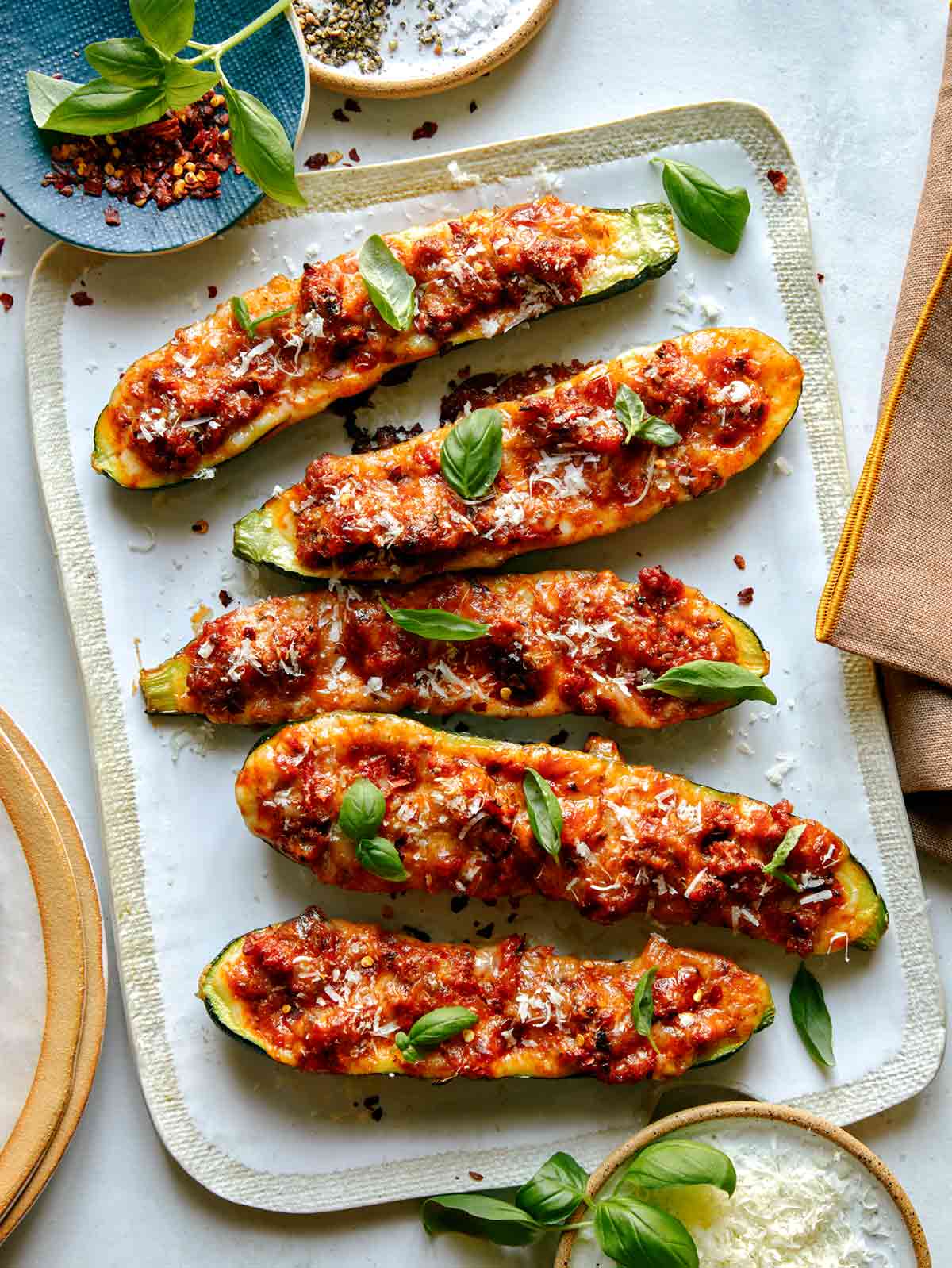 Zucchini boats on a platter with basil and parmesan on the side. 
