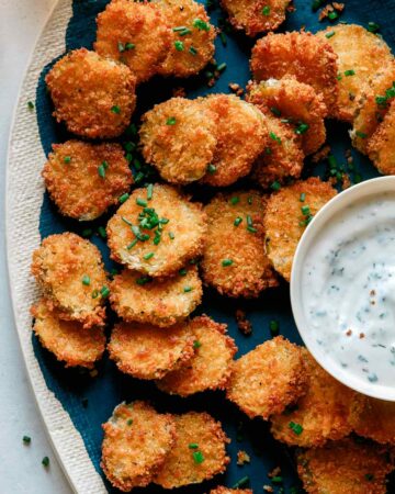 Fried pickle chips on a platter with ranch dressing.