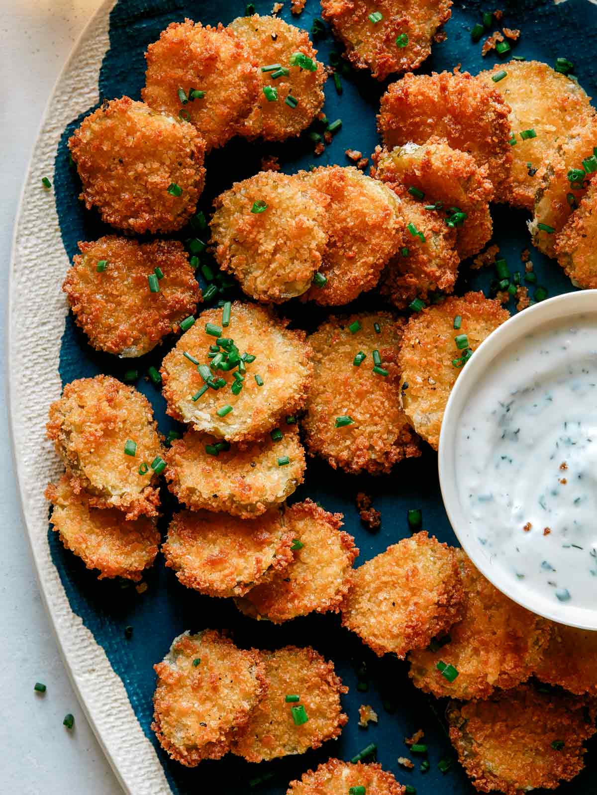 Fried pickle chips on a platter with ranch dressing. 