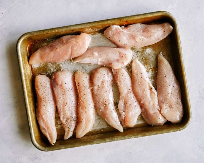 Chicken tenders being seasoned.