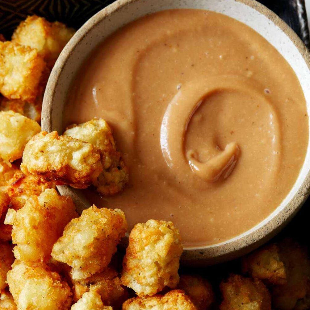 A bowl of homemade chick fil a sauce with a lot of tater tots on the side.