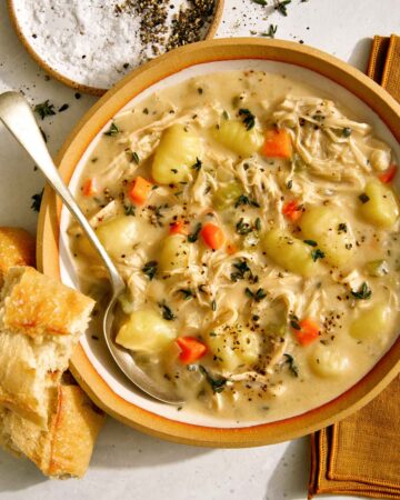 Chicken and gnocchi soup in a bowl with bread on the side.