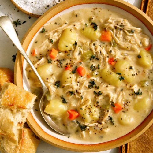 Chicken and gnocchi soup in a bowl with bread on the side.