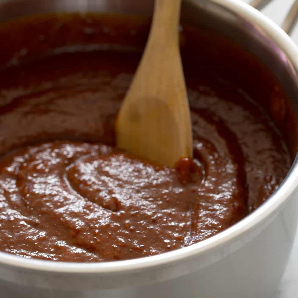 A pot of sweet and tangy BBQ sauce being stirred by a wooden spoon.