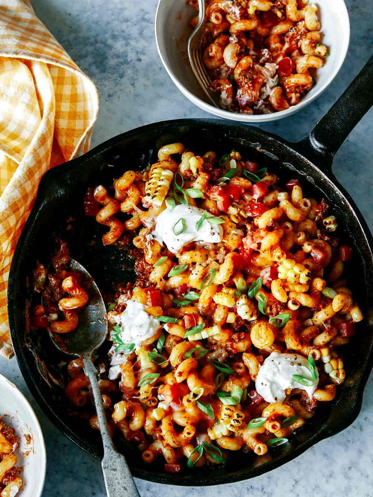 Taco pasta in a skillet with a spoon and a serving in a bowl.