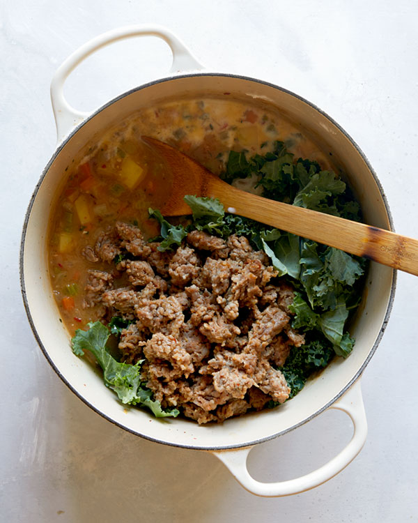 Adding in sausage, kale, and milk to make a soup recipe. 