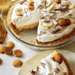 A slice of banana cream pie on a plate with the pie in the background.