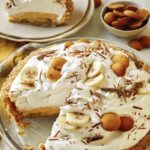 A slice of banana cream pie on a plate with the pie in the background.