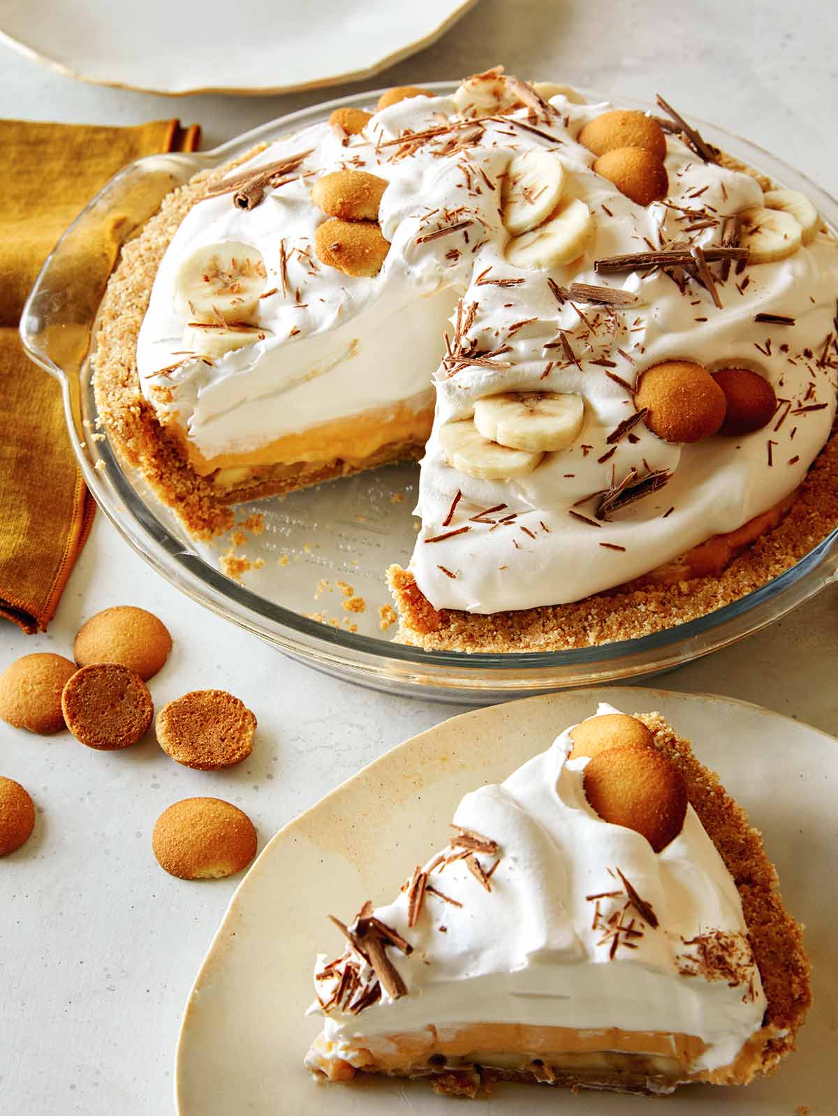 A slice of banana cream pie on a plate with the pie in the background. 