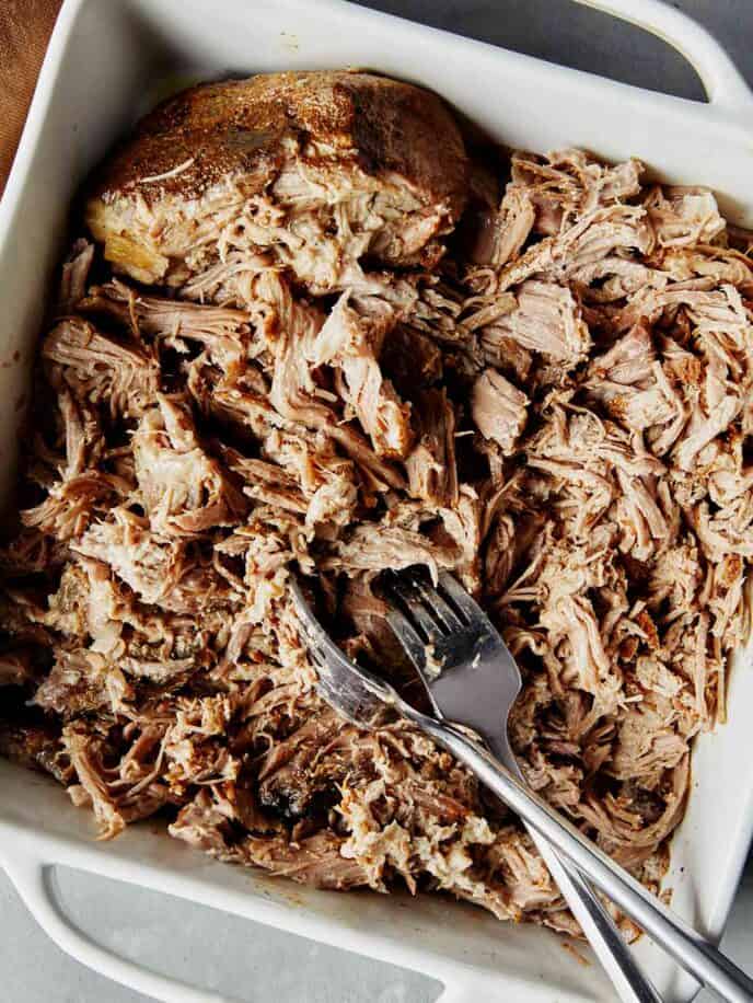 Pulled pork being shredded in a baking dish. 