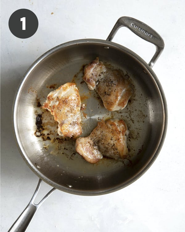 Seared chicken thighs in a skillet with salt and pepper.