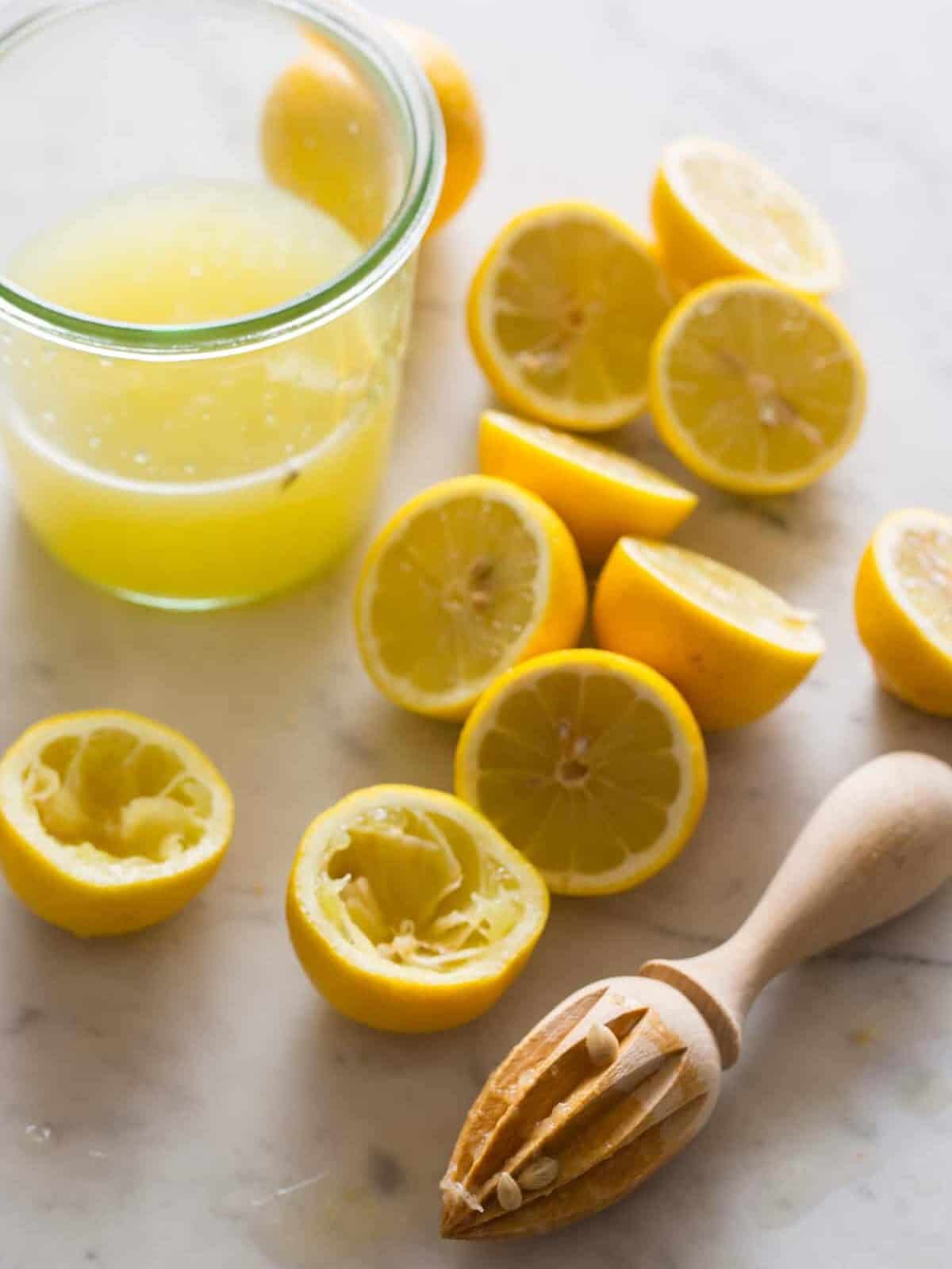A glass of lemon juice, lemon halves, and a wooden citrus juicer.
