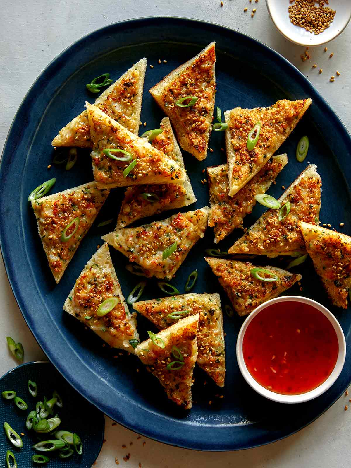 Shrimp toast recipe on a platter with green onions and sesame seeds. 