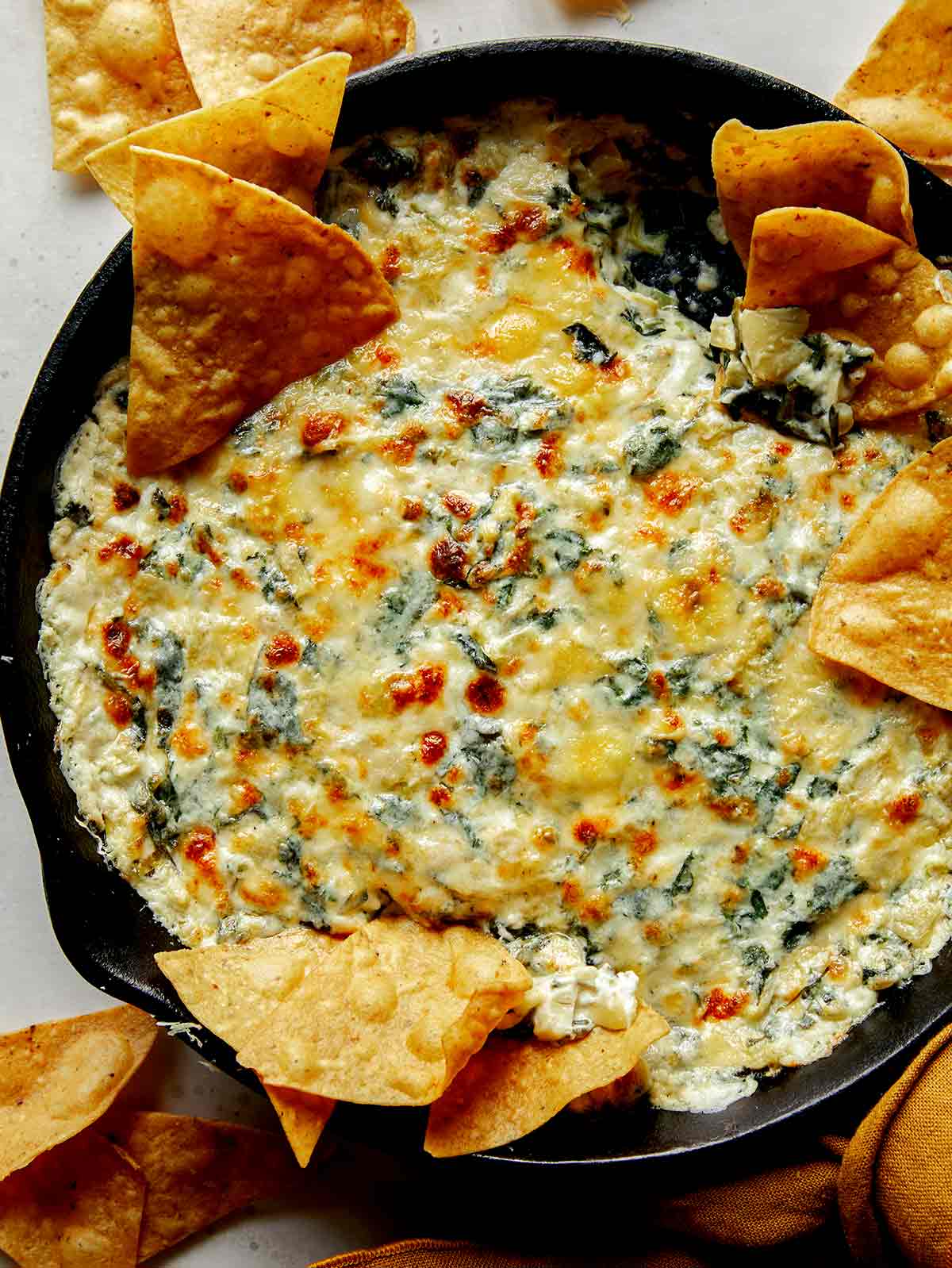 Spinach and artichoke dip in a pan with tortilla chips on the side. 