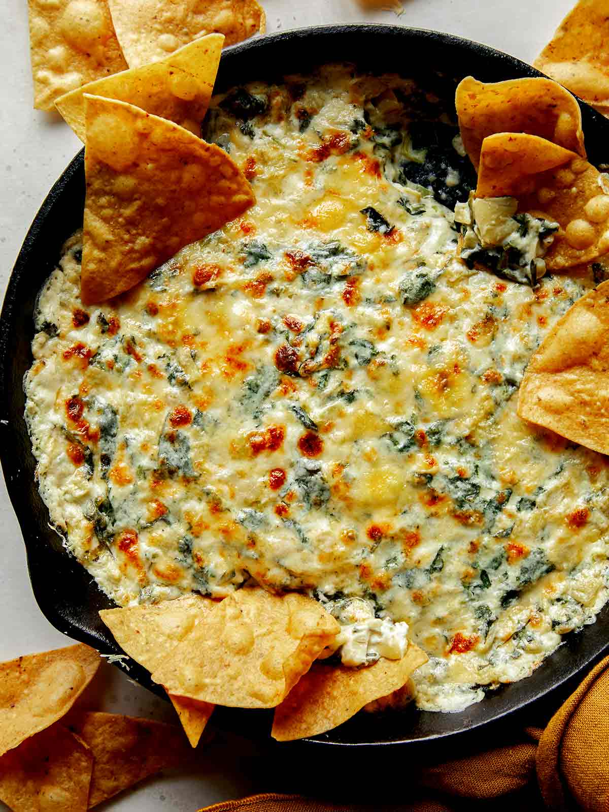 Spinach and artichoke dip in a pan with tortilla chips on the side.