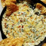Spinach and artichoke dip in a pan with tortilla chips on the side.