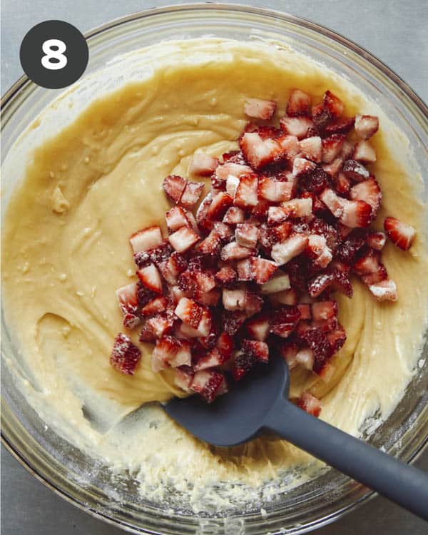 Muffin batter in a glass bowl with strawberries added in on top.