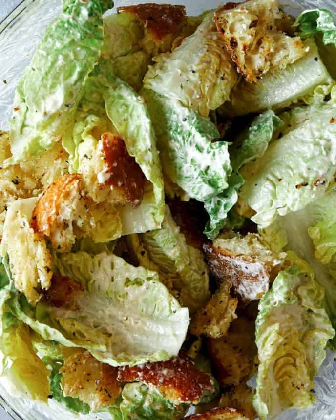 Croutons being mixed in with lettuce to make a salad. 