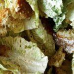 Croutons being mixed in with lettuce to make a salad.