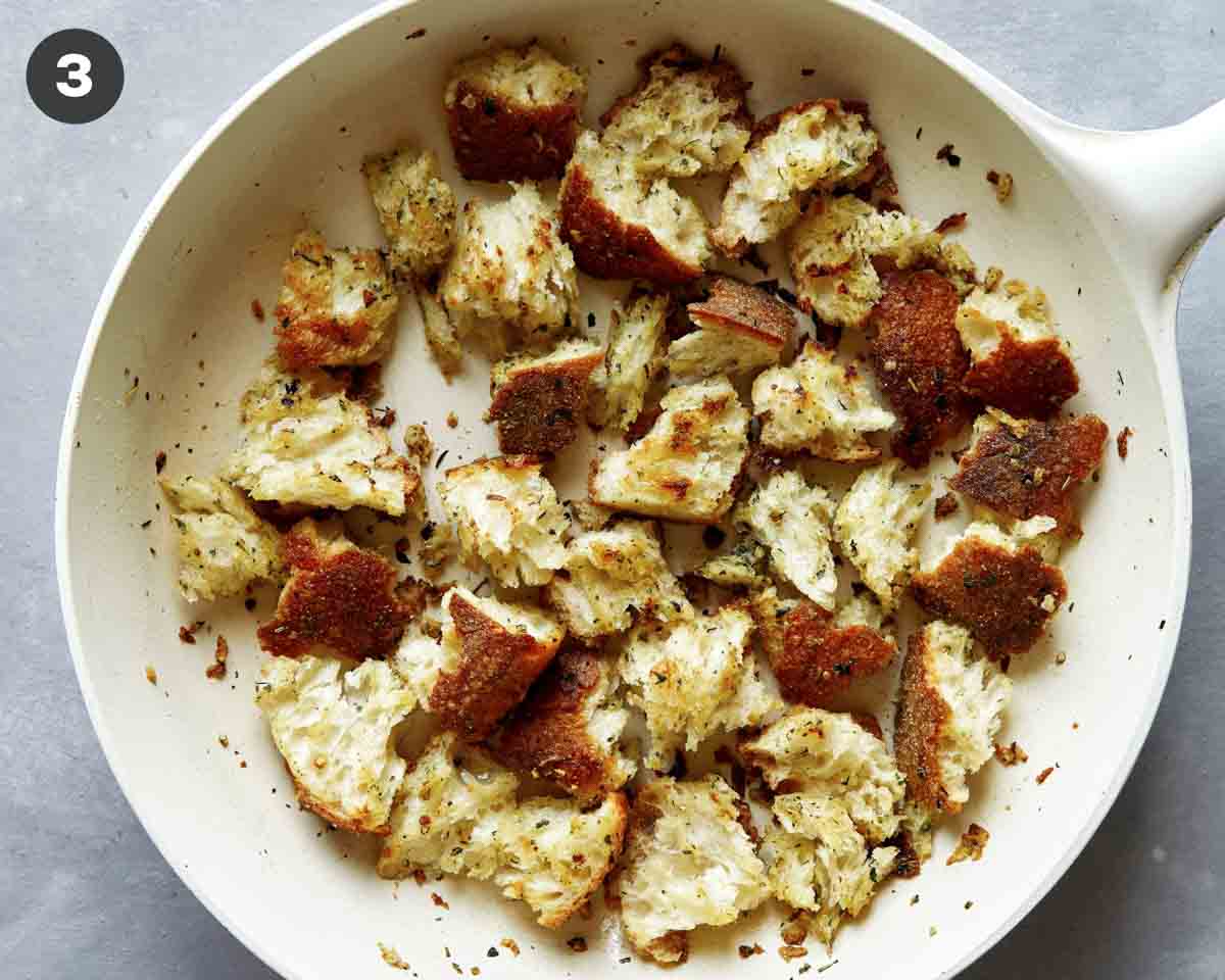 Torn bread croutons in a skillet toasting. 