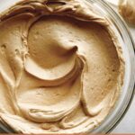 A big bowl of peanut butter frosting with a spatula next to it.