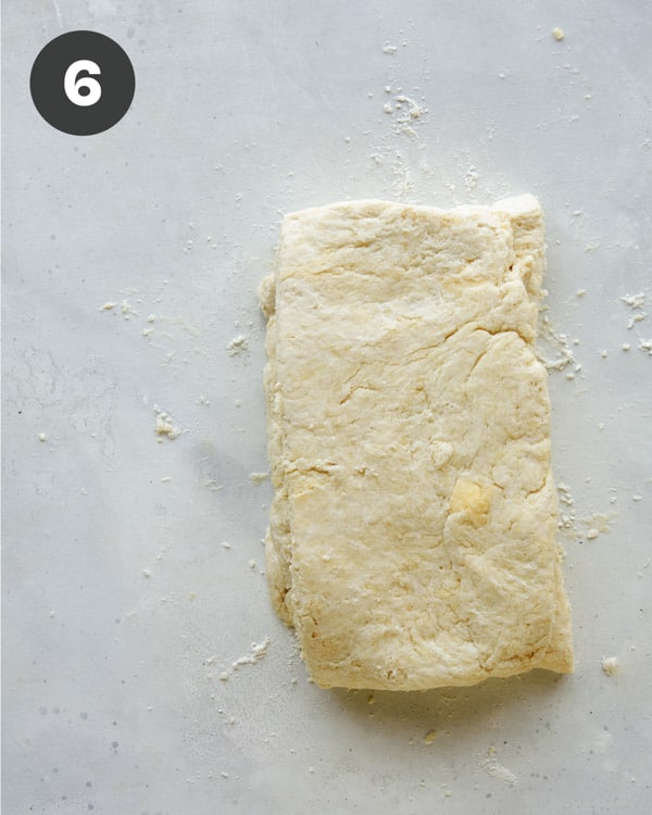 Biscuit dough being folded in half on a surface.