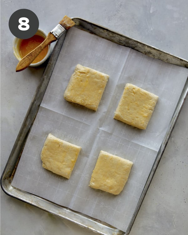 Biscuits on a baking sheet being brushed with butter. 