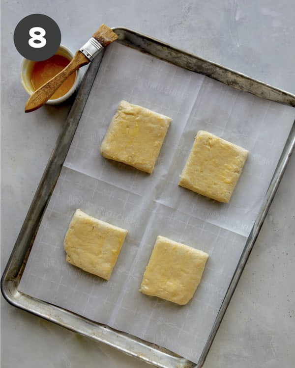 Biscuits on a baking sheet being brushed with butter.