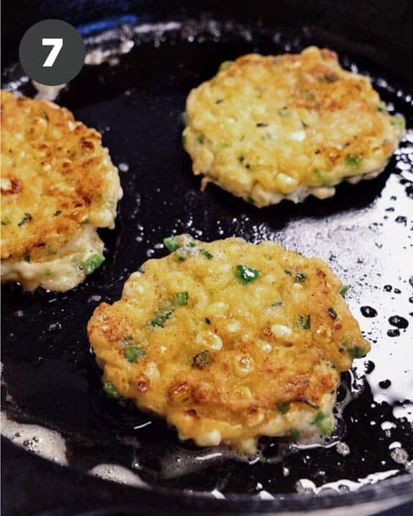 Corn cakes in a skillet after being flipped. 
