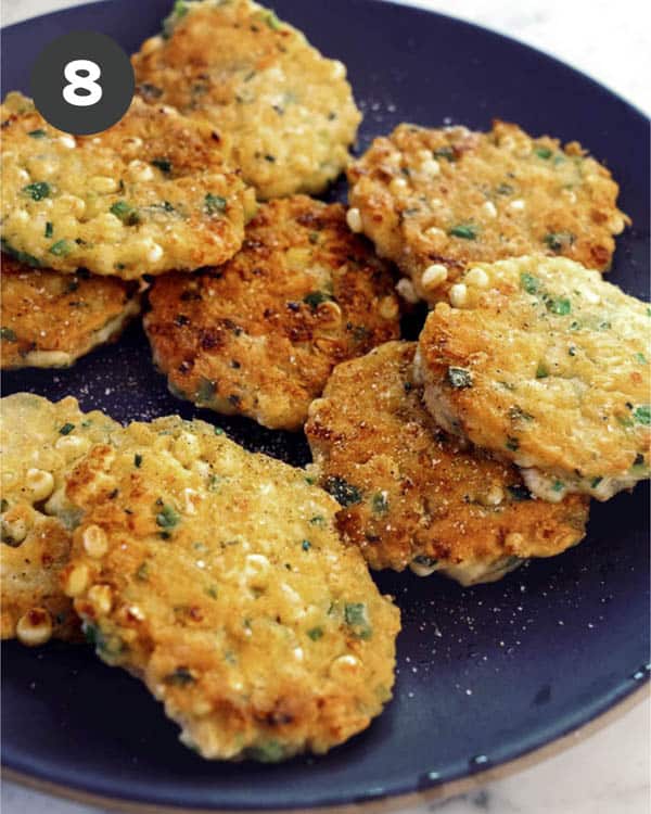 Corn cakes on a platter seasoned  with salt and pepper. 