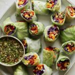 A platter of fresh spring rolls with a dipping sauce.