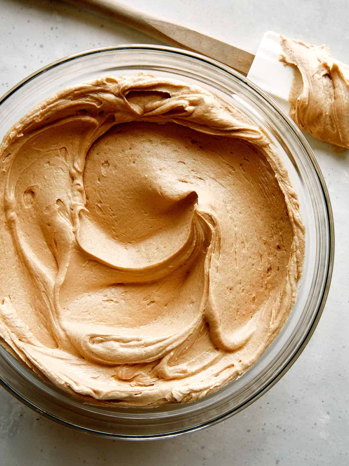 A big bowl of peanut butter frosting with a spatula next to it. 