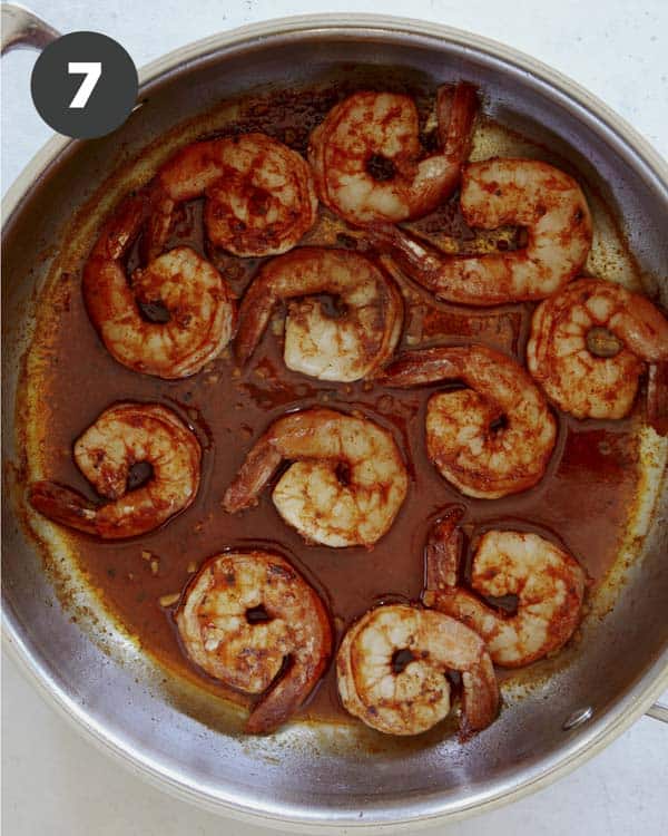 Shrimp cooking in a skillet with seasoning.