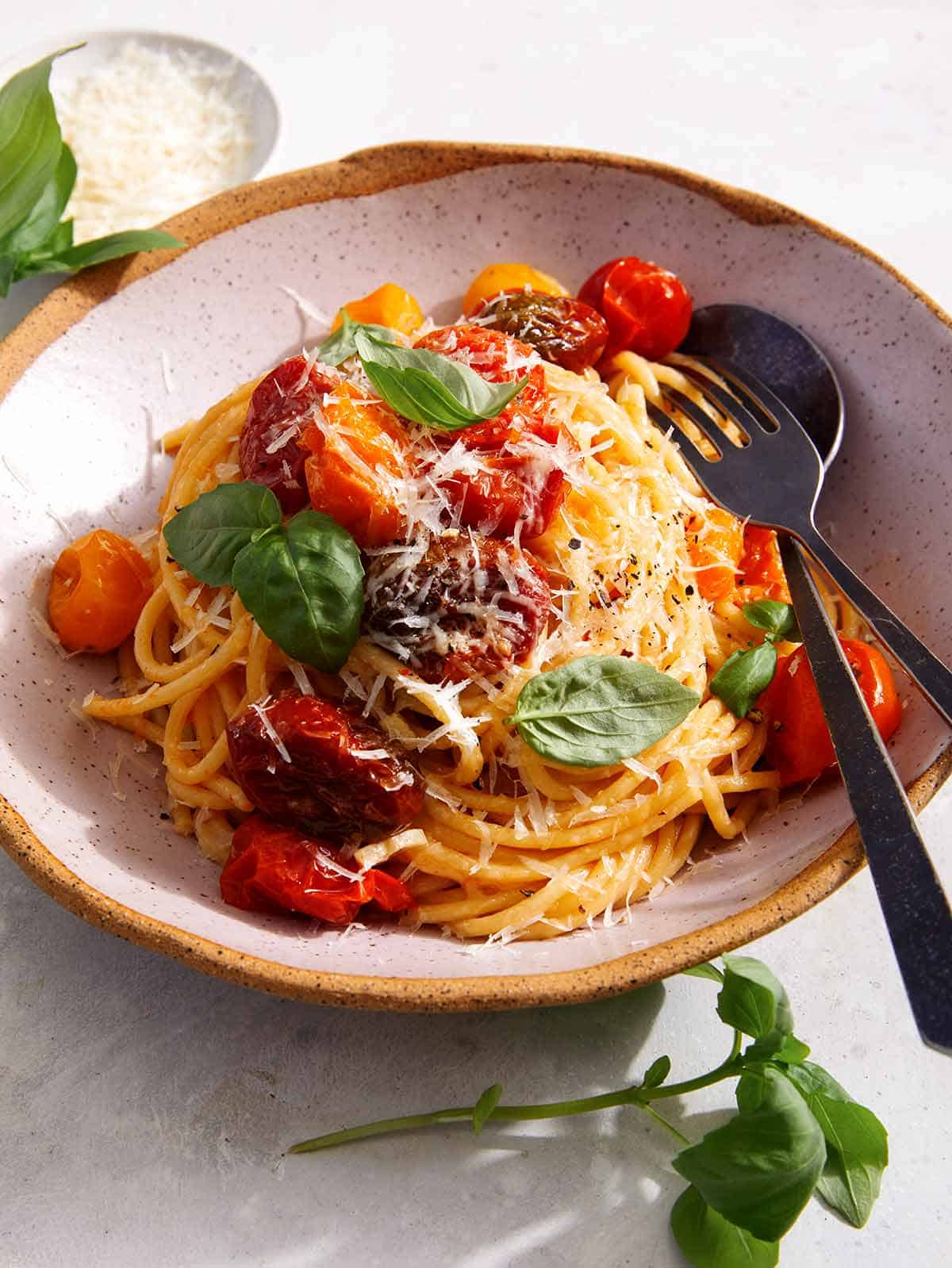 Butter roasted cherry tomato pasta recipe in a bowl with basil on the side. 