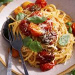 Butter roasted cherry tomato pasta recipe in a bowl with basil on the side.