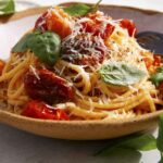 Butter roasted cherry tomato pasta recipe in a bowl with basil on the side.