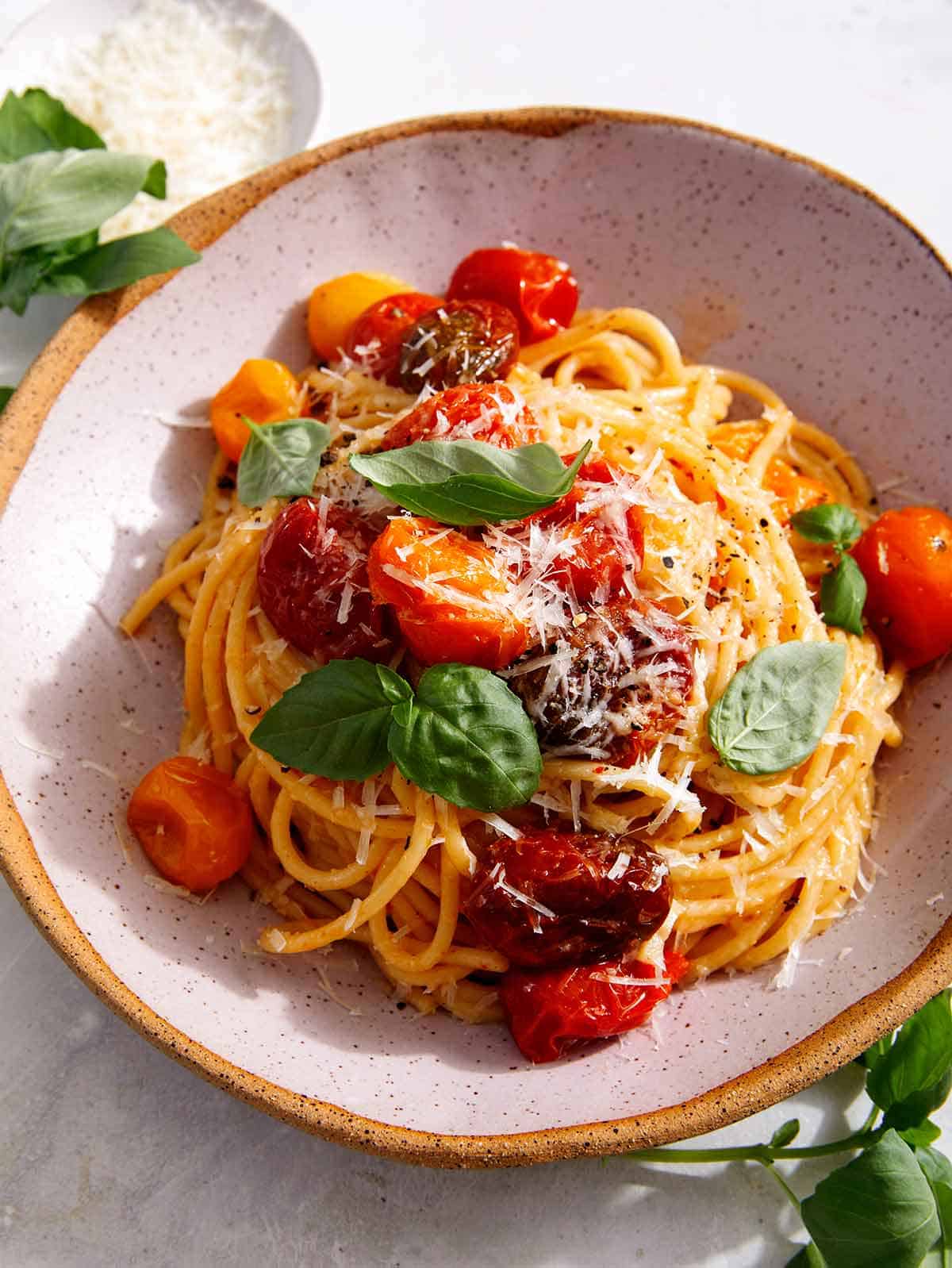 Butter roasted cherry tomato recipe in a bowl with some basil on the side.