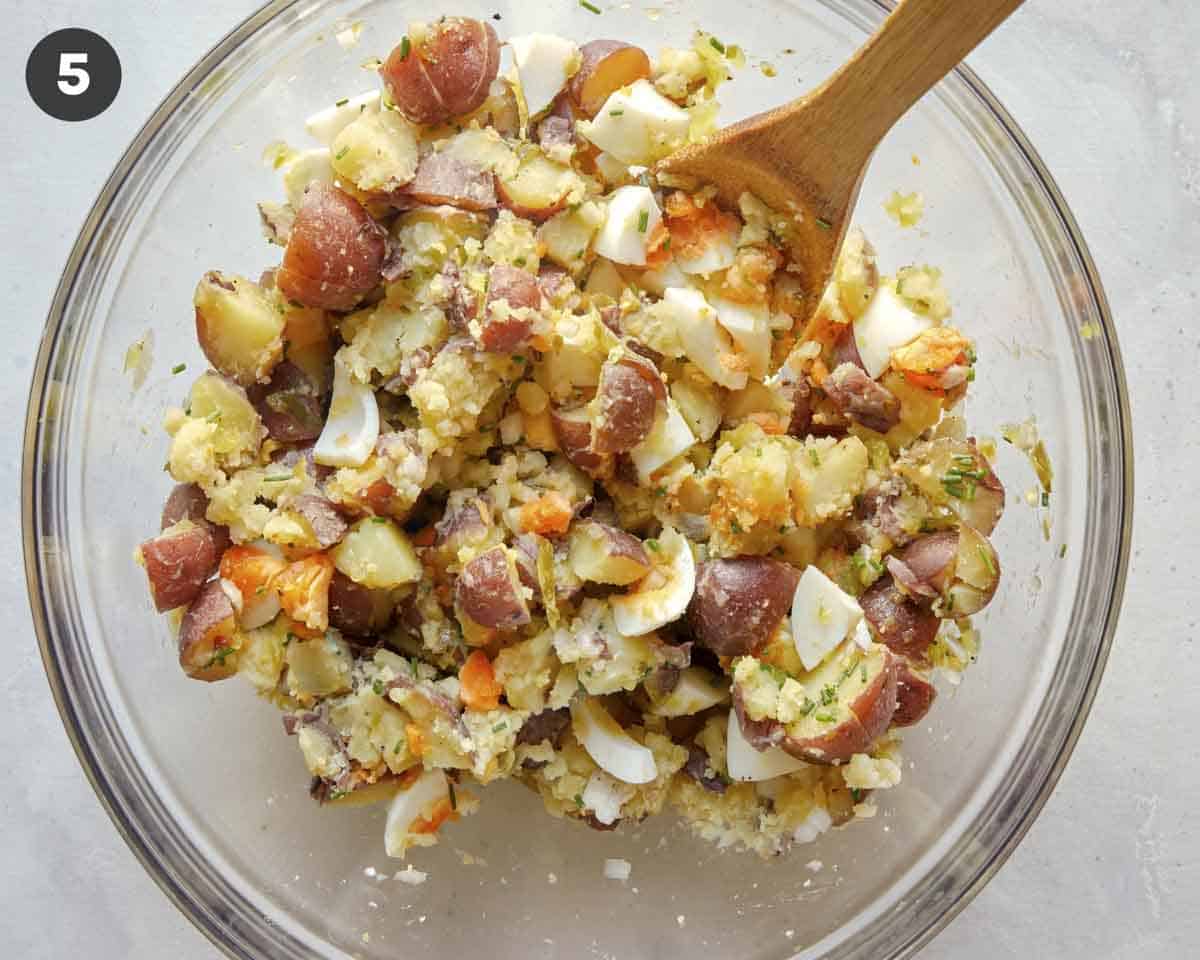 Potato salad with hard boiled eggs and potatoes being mixed in a bowl.